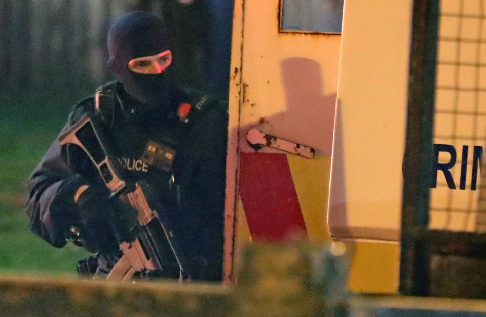 An armed officer looks out from beside a police armoured vehicle as riots erupt in Londonderry