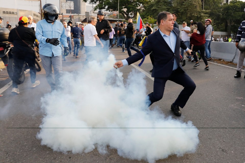  An opponent to President Maduro throws a tear gas canister back at state troops