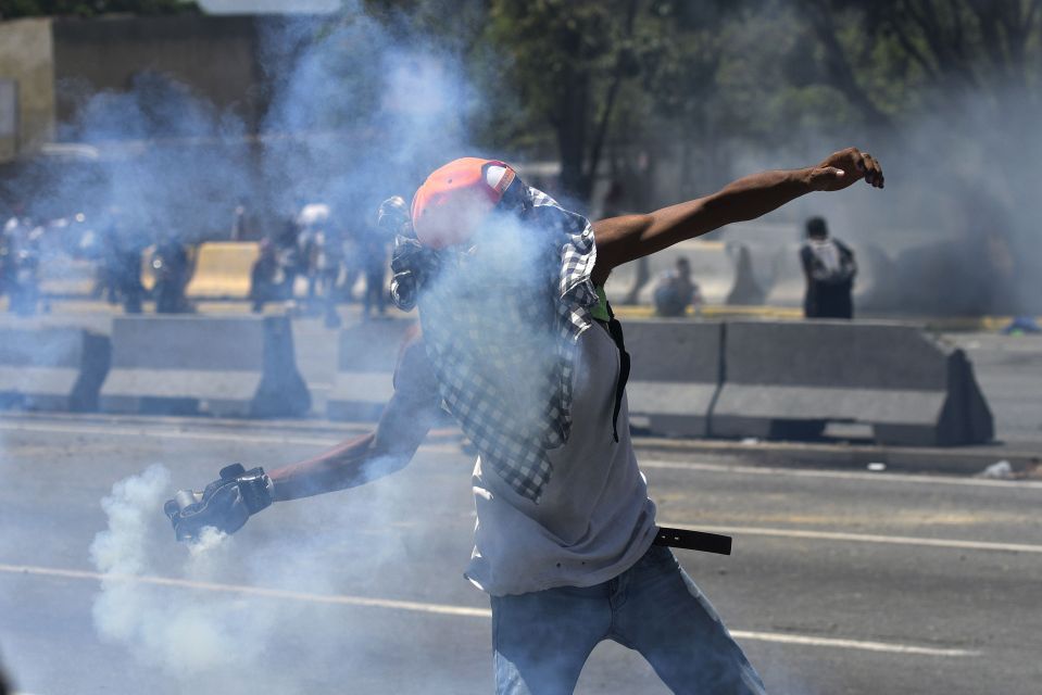  A demonstrator throws a tear gas canister back at government troops