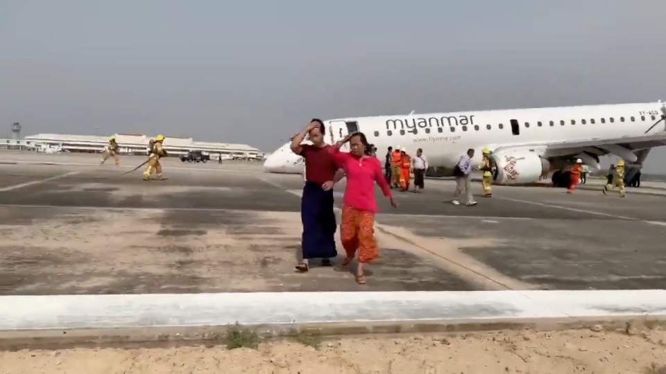 Passengers walk away from the plane after Myanmar National Airlines flight UB103 landed without a front wheel