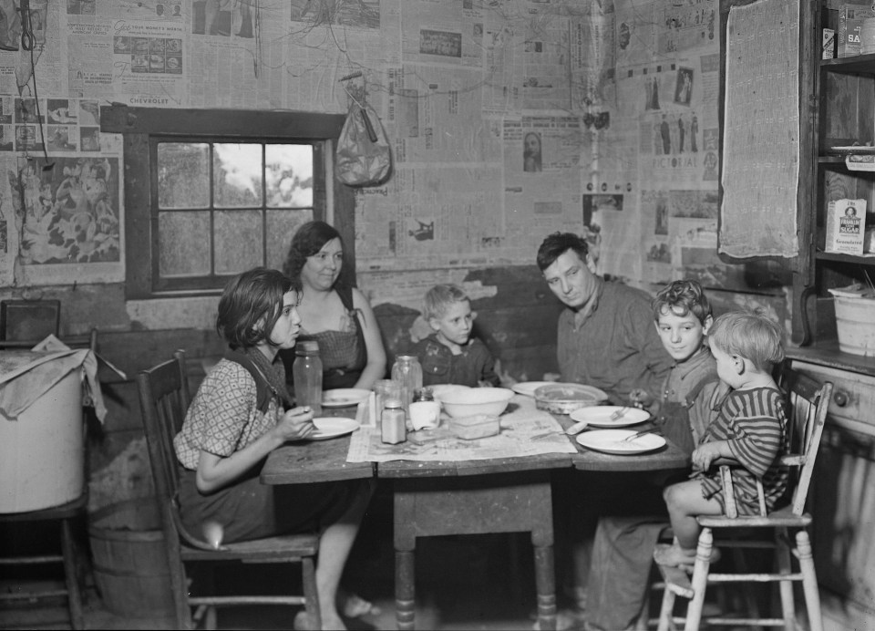 A family sits down for supper – there’s not much to go around and it appears newspaper has been put up in lieu of wallpaper