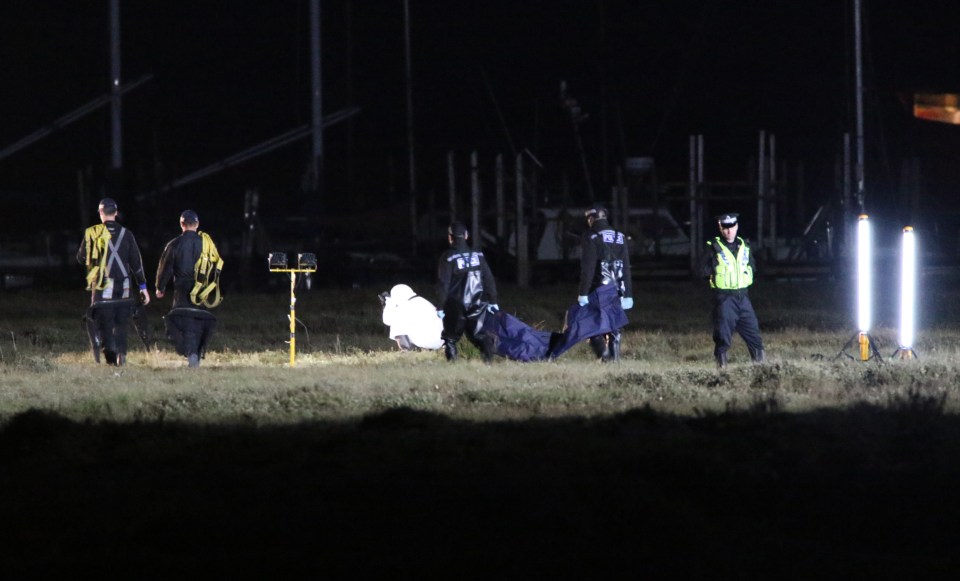 Cops haul a body bag over to the forensic team