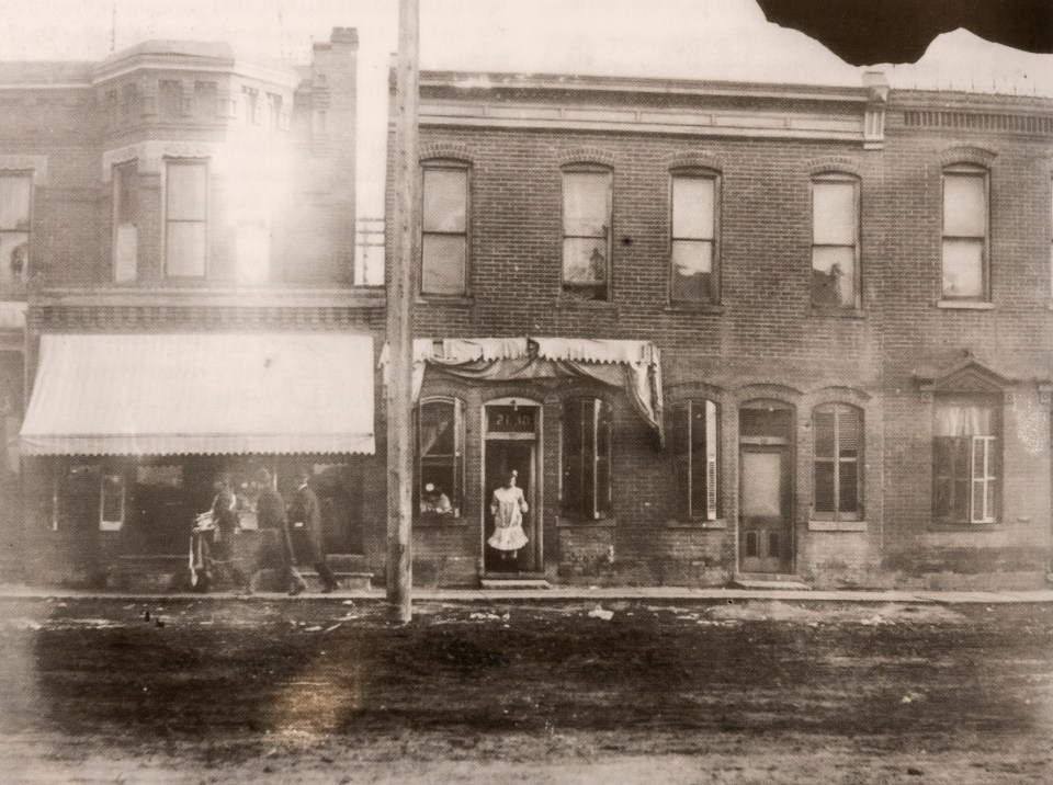  Two women wearing white brothel gowns are seen in the facade of 2130 Market Street, Denver, 1905, as three men wander down the mud-filled filthy street 