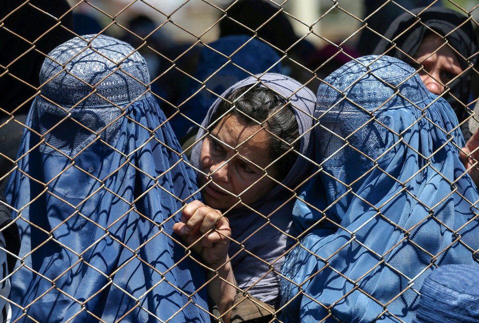  Women in Afghanistan wait behind a wire fence