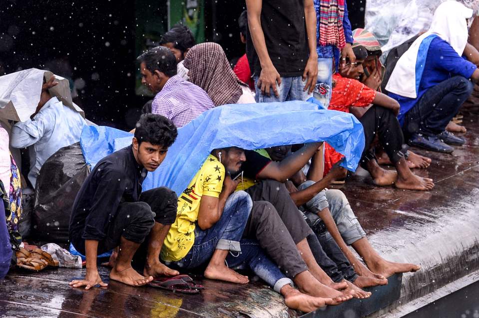 Bangladeshis cover themselves from the rain as they wait for the next train to arrive