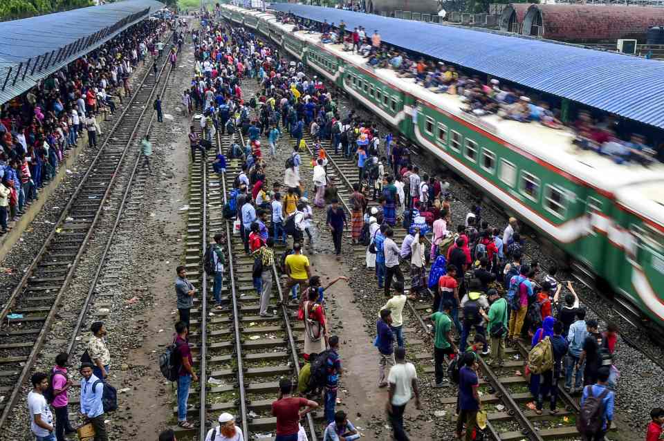 People try to leap onto a moving train as it passes through the station at Dhaka