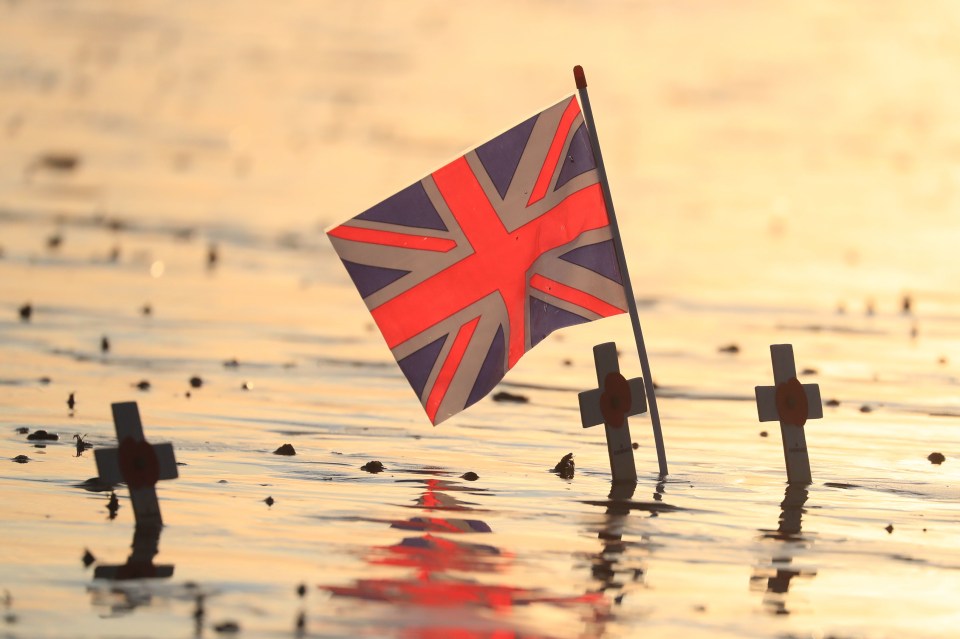 Crosses of remembrance placed alongside a Union flag at dawn on the beach at Arromanches in Normandy