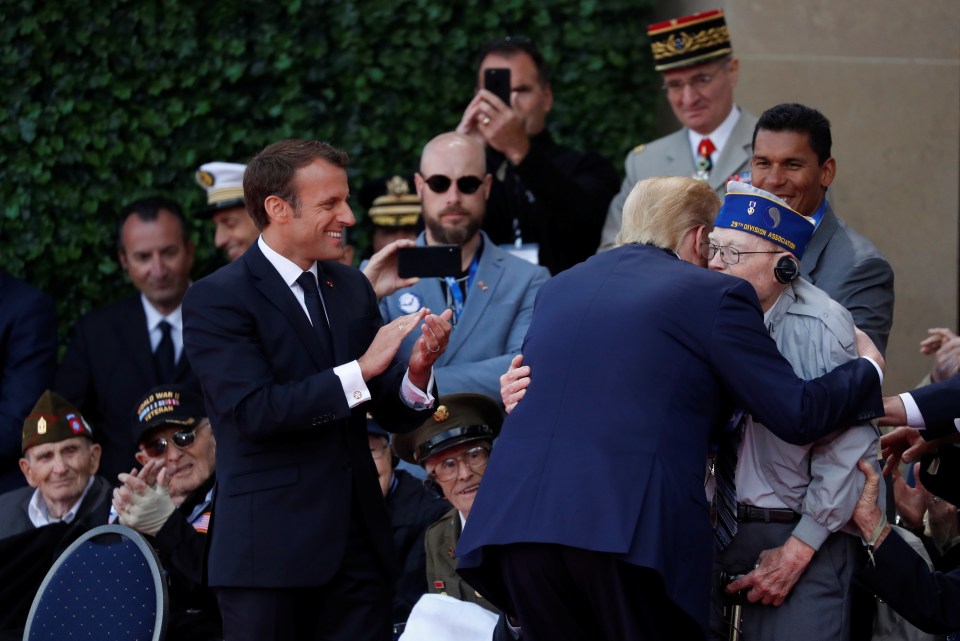 President Trump hugs a US military veteran while French President Emmanuel Macron smiles and applauds the gesture