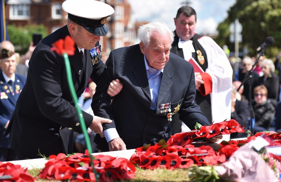 A veteran is aided as he lays a poppy wreath at the D-Day Stone at the ceremony in Portsmouth