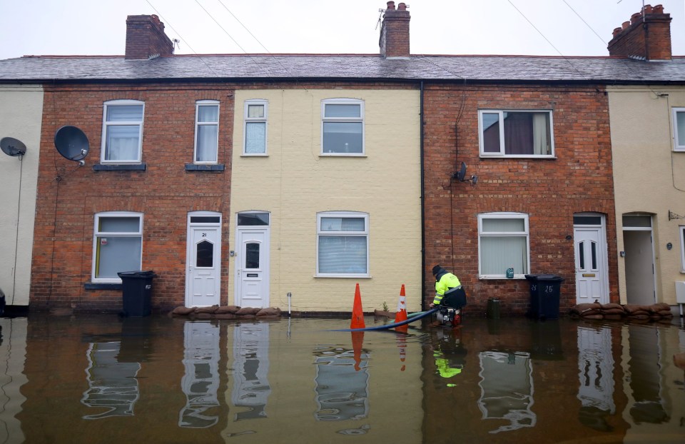 People attempt to protect their homes with sandbags in Mancot as a worker tries to pump away the floodwater