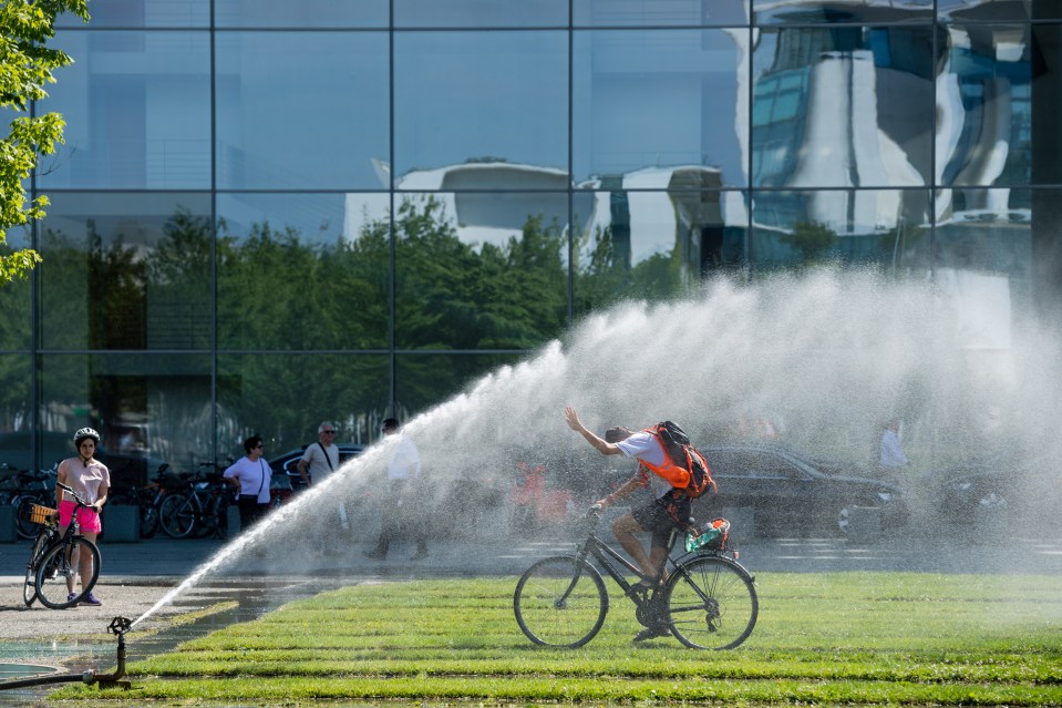  A man rides his bicycle under the water jet of a sprinkler system in Berlin, Germany, today