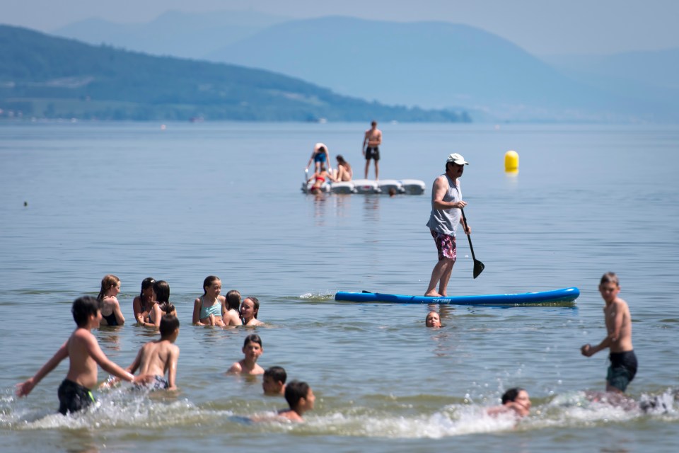  A man practices paddle board as children play in the water of the Lac de Neuchatel to cool off during the sunny and warm weather, in Yverdon-les-Bains, Switzerland