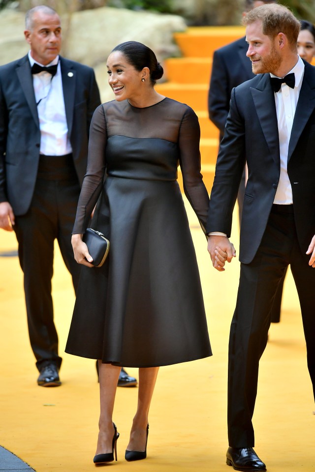  Meghan smiles at well-wishers while on the red carpet as she holds Prince Harry's hand