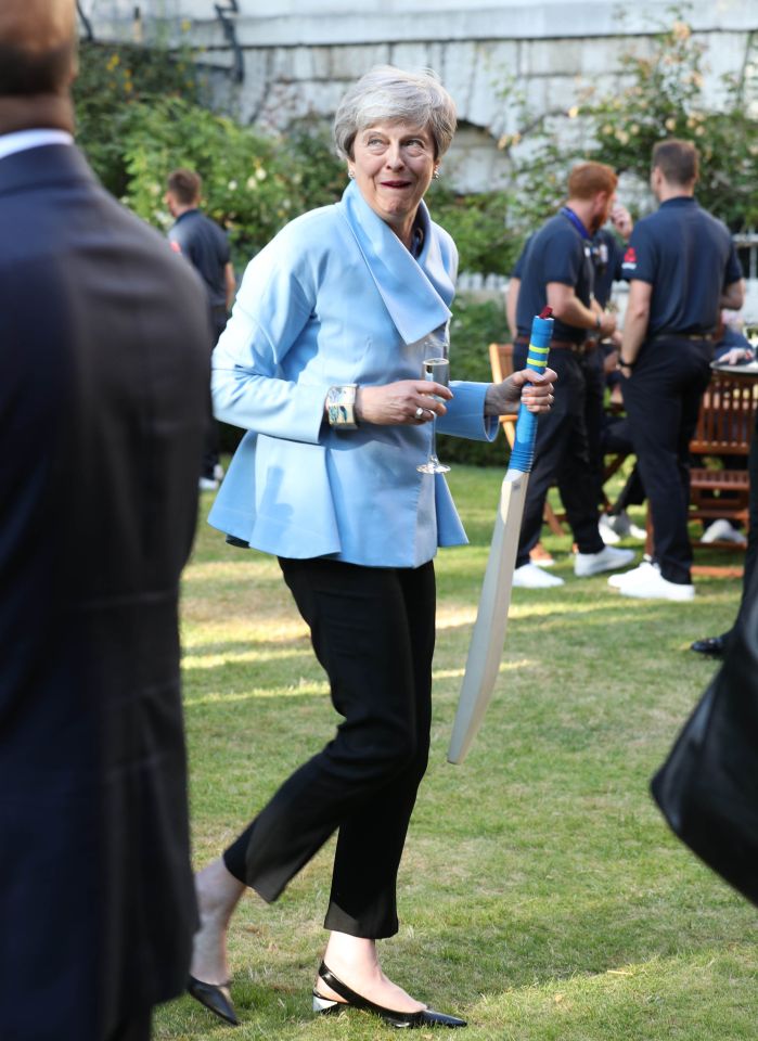  Avid cricket fan Theresa May grins as she holds a bat and a glass of champers at the party