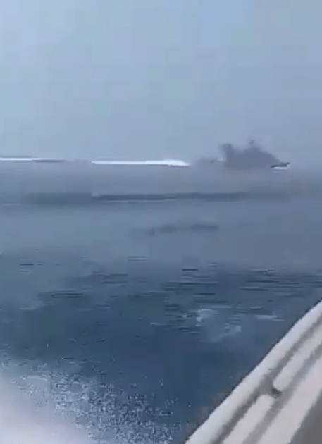  Video footage seemingly shows a warship sailing in the distance while a group of smaller boats follow behind at a distance