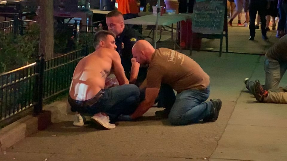  Emergency workers and an unidentified person, left, tend to an injured person on the sidewalk after the deadly shooting