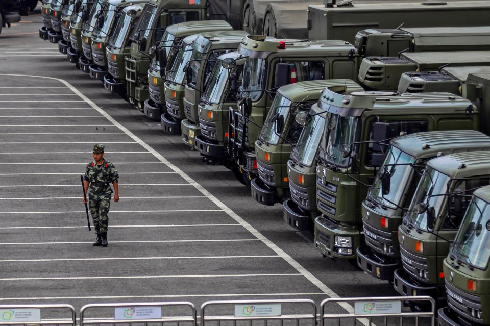  A member of People's Armed Police Force (PAP) walks by military vehicles