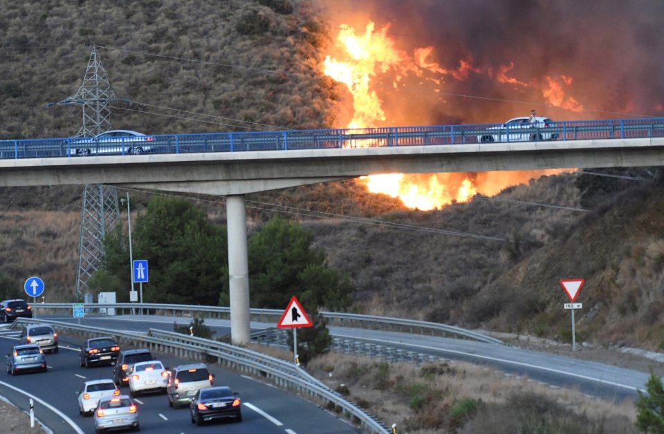  A view of the fire burning next to cars passing across a major road