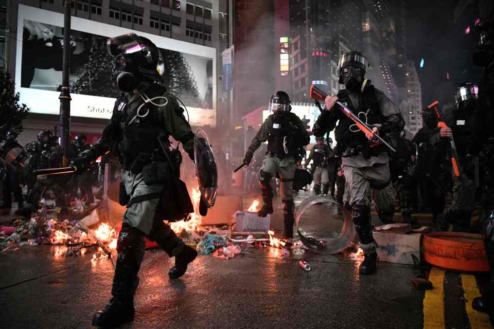  Police run past debris set alight by protesters in the Causeway Bay area