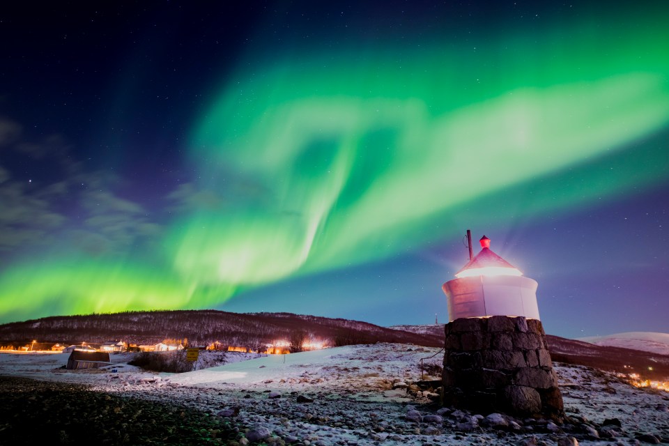  Aurora borealis or northern lights are visible in the sky above a lighthouse to the village of Strand near Tromso in Norway