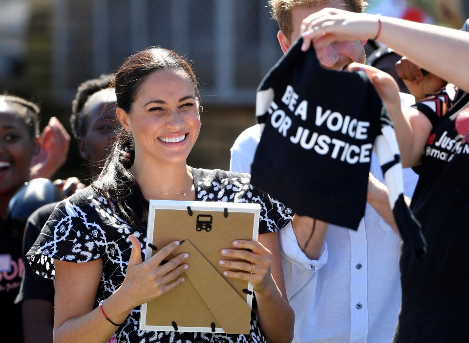  Meghan cracks a smile as a tiny T-shirt is gifted to Archie, with a slogan 'be a voice for justice'