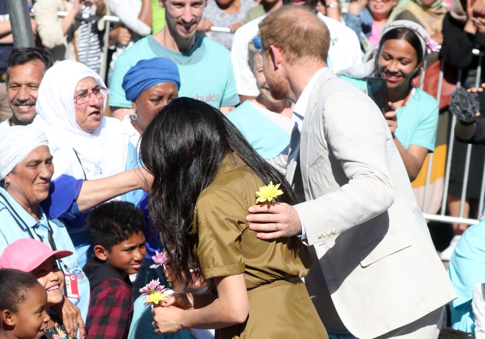  Prince Harry holds a yellow flower given to him from a fan as he puts a hand on Meghan's back