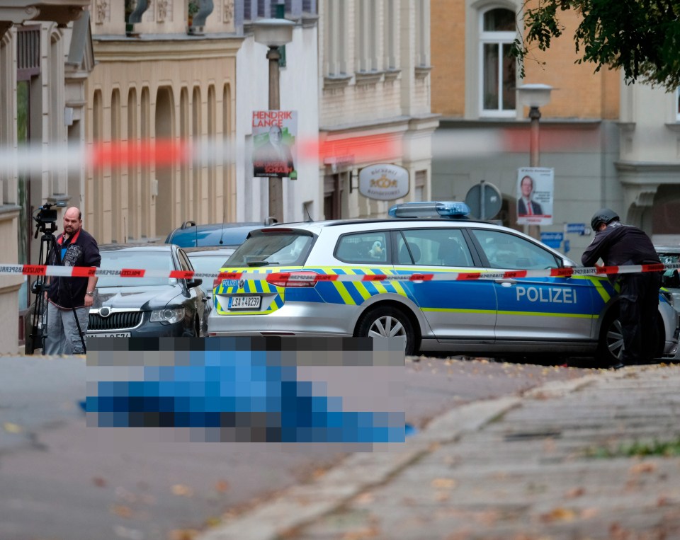 A body laying in the street is covered as police block the area around the site of a shooting