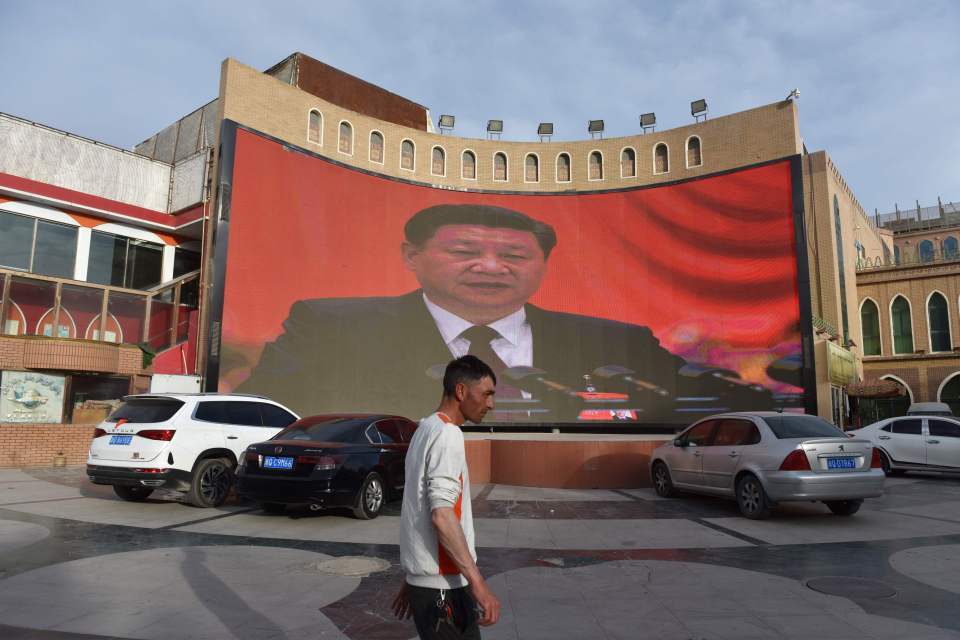  A man walking past a screen showing images of China's leader Xi Jinping in Xinjiang