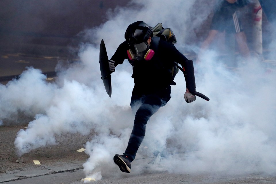  An anti-government protester runs through a cloud of tear gas