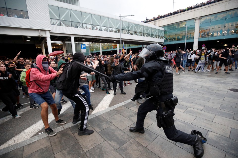  A riot cop swings his baton at protesters outside the airport amid clashes following the sentencing of a dozen Catalan leaders