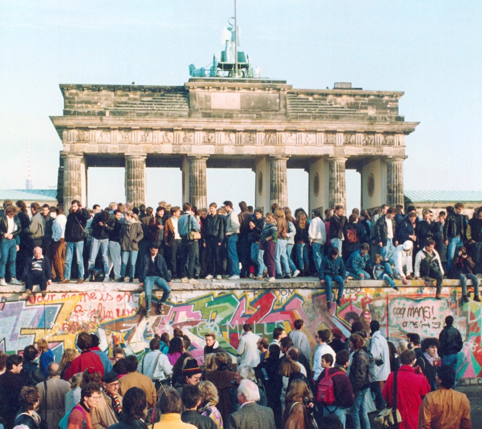  Germans from East and West stand on the Berlin Wall in front of the Brandenburg Gate in Berlin