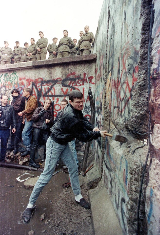  A demonstrator pounds away the Berlin Wall as East Berlin border guards look on from above the Brandeburg Gate in this November 11, 1989