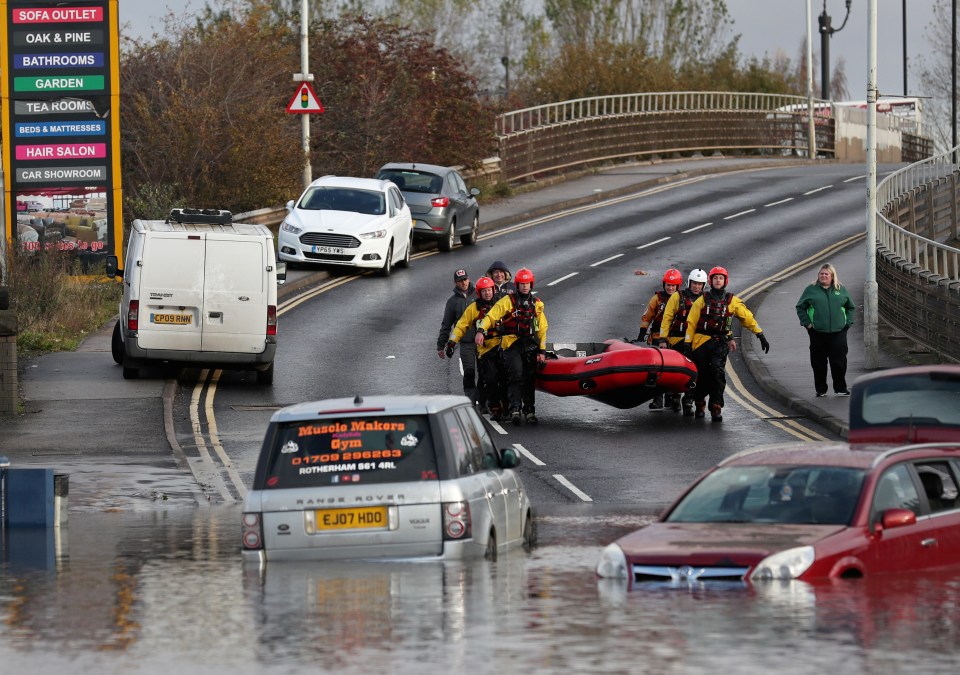  Rescuers carry an inflatable raft as the cars sit in floodwater in Rotherham, near Sheffield