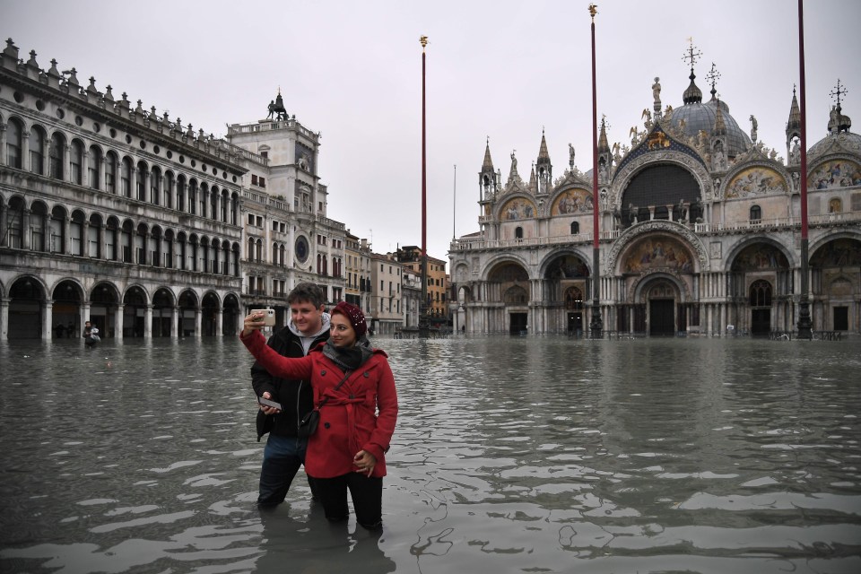 People take selfies at the flooded St. Mark's square by St. Mark's Basilica