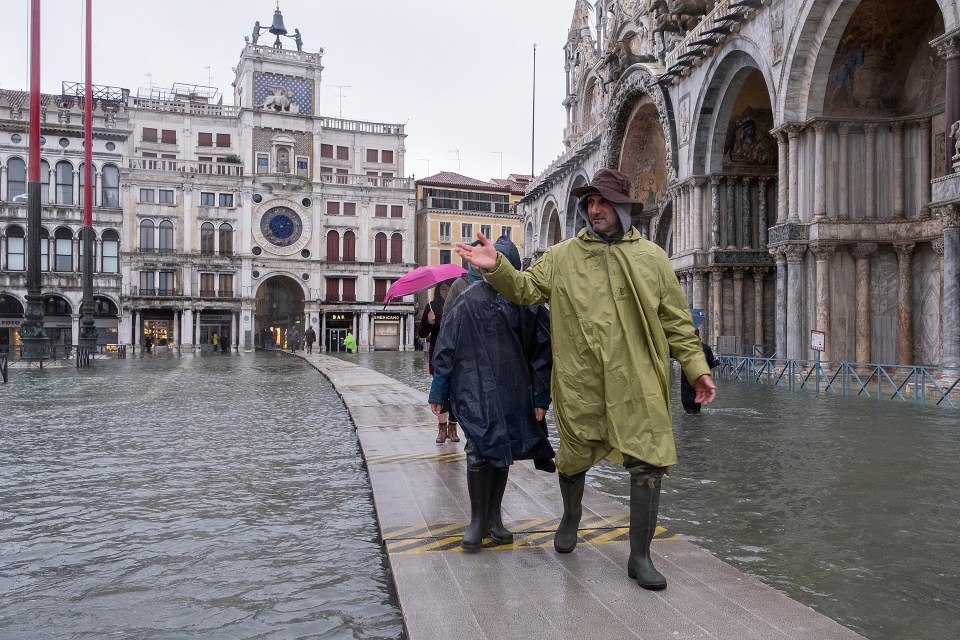 Tourists walk on temporary raised walkways in the Piazza San Marco