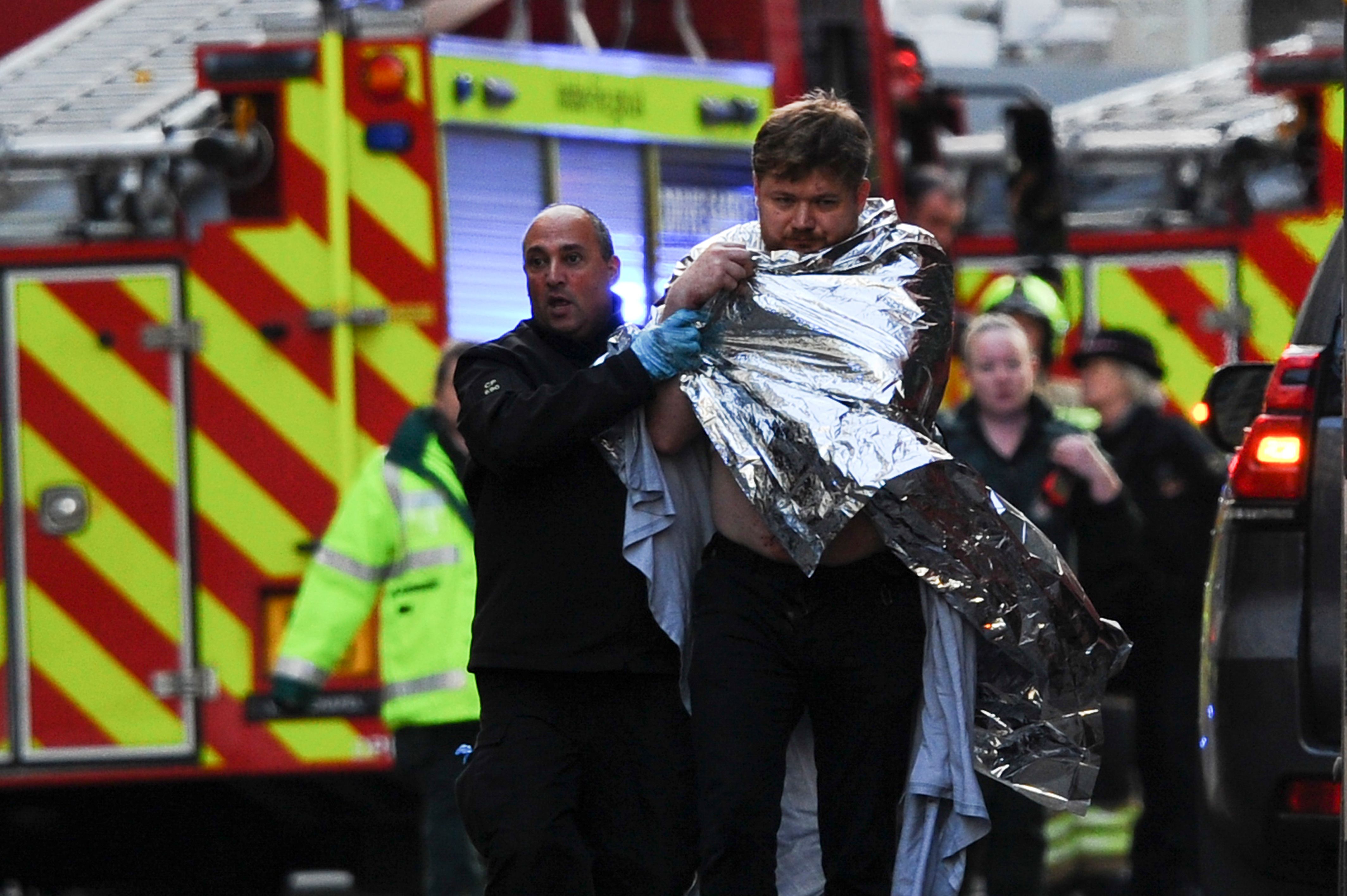  A man is bundled away from the scene wrapped in a blanket