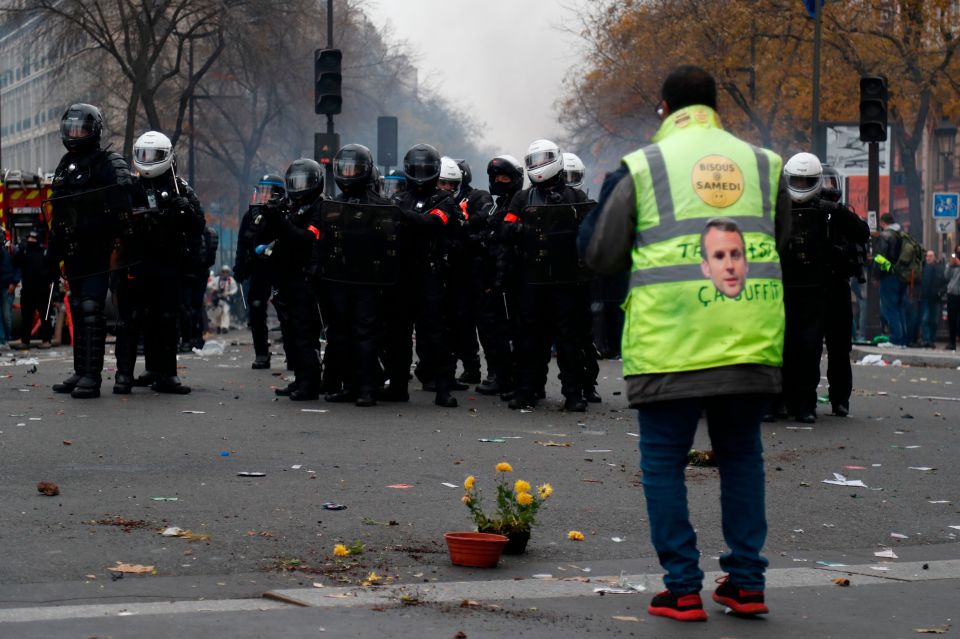  A protester stands opposite armed police wearing a jacket with Emmanuel Macron's face tacked onto it