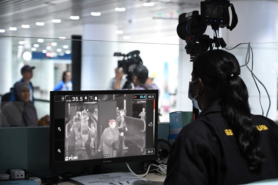 A Malaysian health officer screens passengers for coronavirus at Kuala Lumpur International Airport