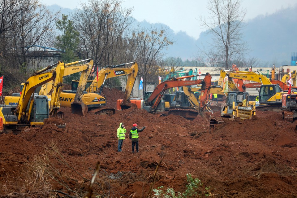  Workers stand amid heavy equipment at a construction site for a field hospital in Wuhan