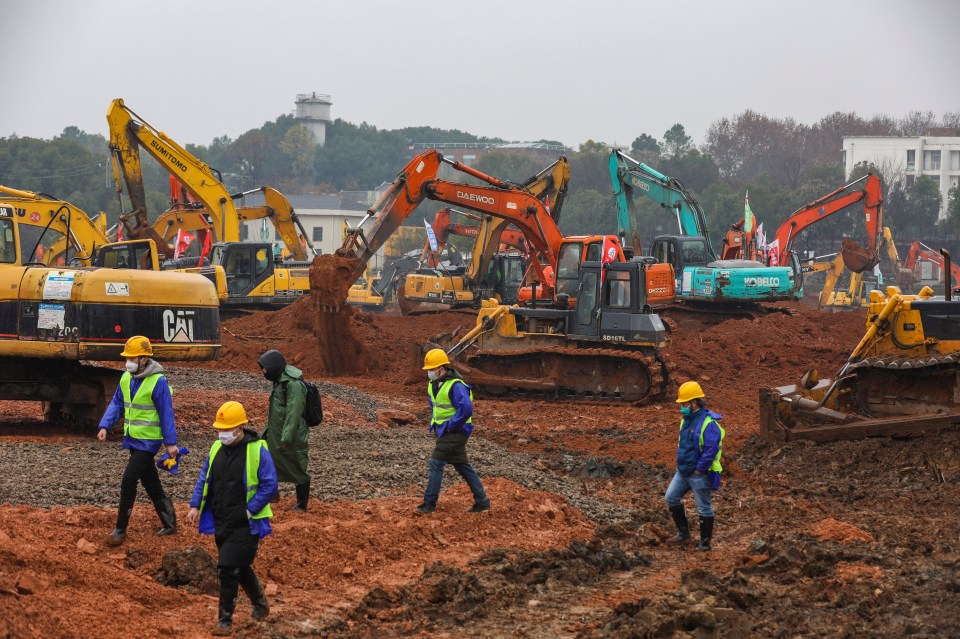  Workers stand amid heavy equipment at a construction site for a 1,000-bed hospital in Wuhan