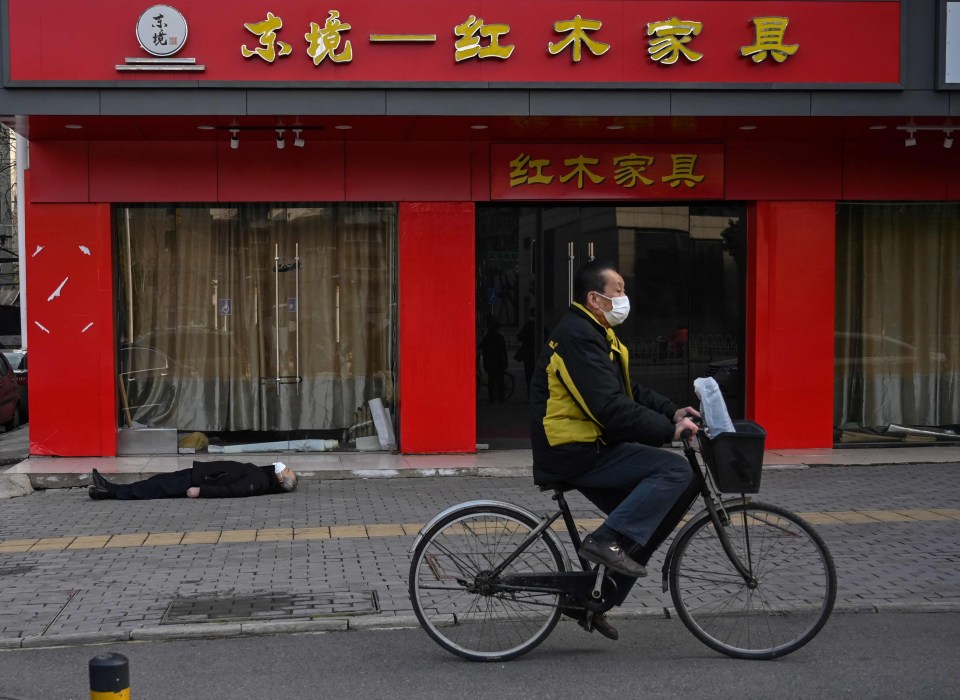 A man wearing a face mask cycles past the body of a man who collapsed and died