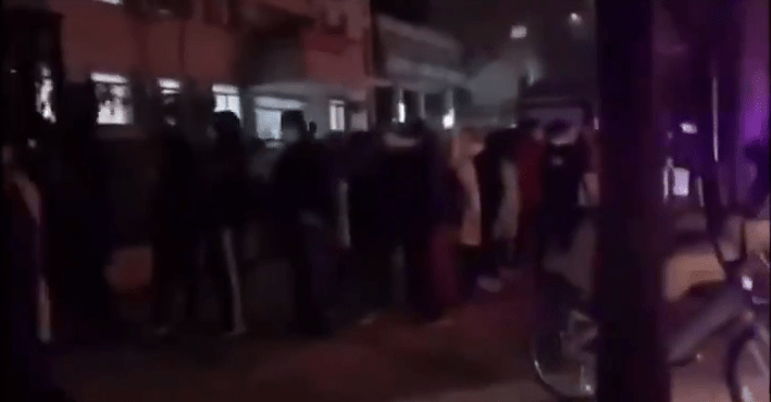 People stand in line on the street waiting to go inside the hospital to see a doctor