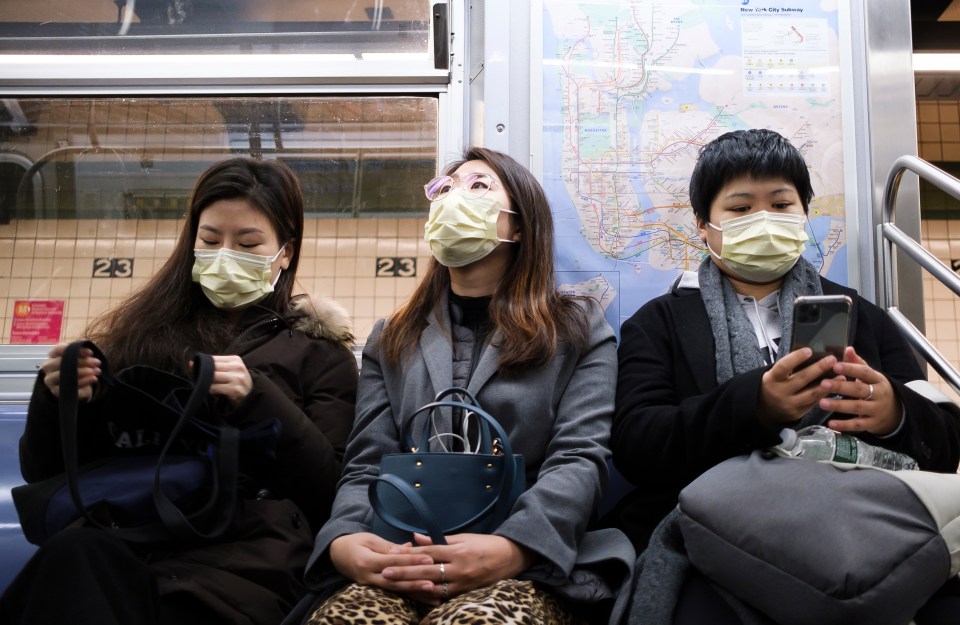  Three people wear masks to cover their faces while riding the subway in New York