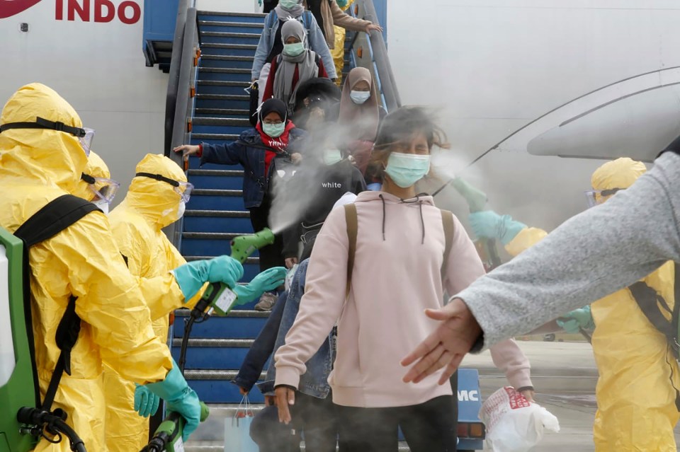  Officials in full protective gear disinfect Indonesian students as they disembark upon the arrival at Hang Nadim international airport in Batam