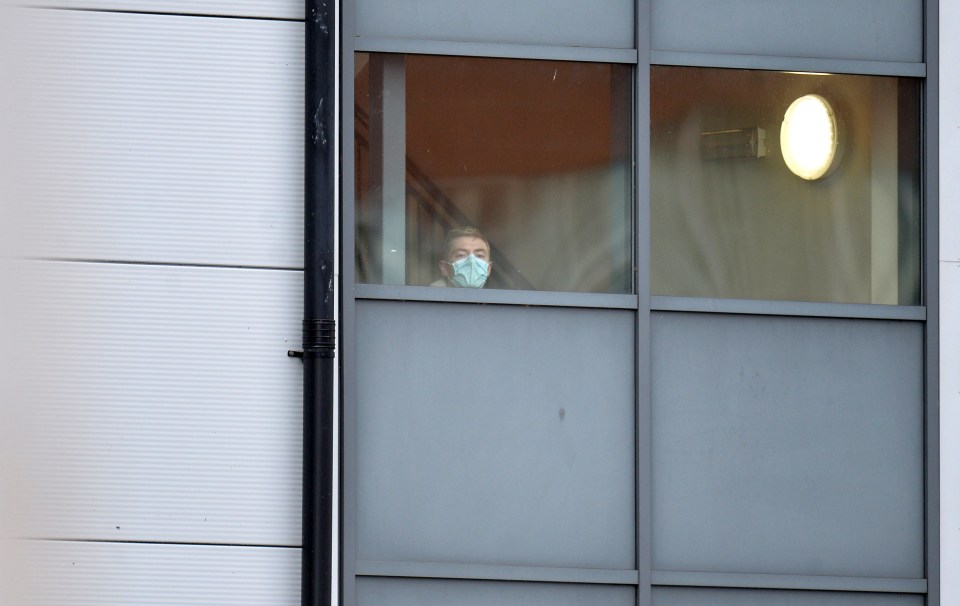  A person wearing a face mask looks out from a window of the accommodation block at Arrowe Park Hospital