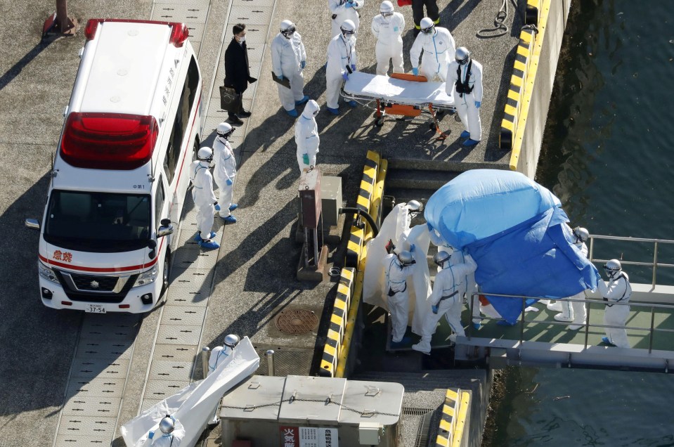 Officers in protective gear escort a person who was on board cruise ship Diamond Princess and tested positive for coronavirus