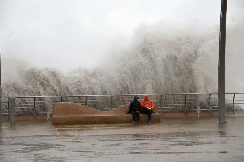  A couple sit along the seafront in Blackpool, with a wall of water behind them