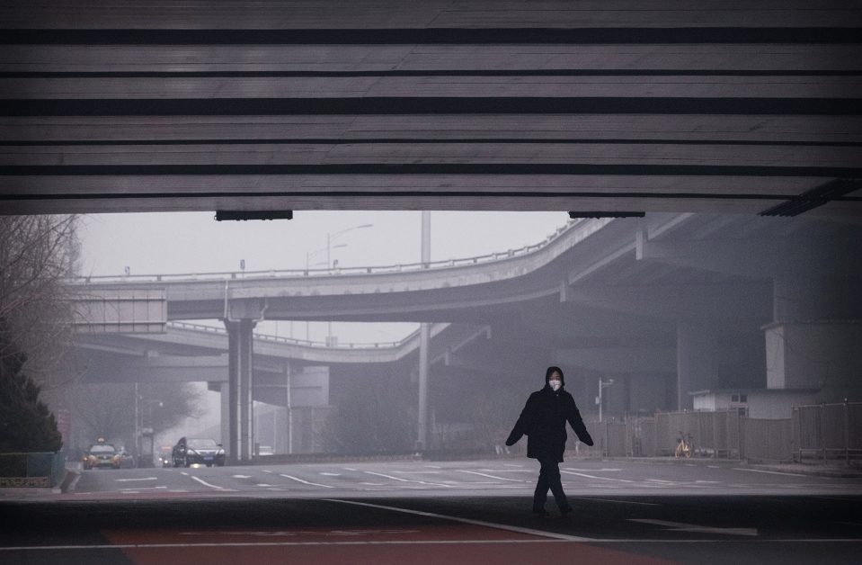  A Chinese woman wears a protective mask as she crosses a nearly empty intersection in Beijing