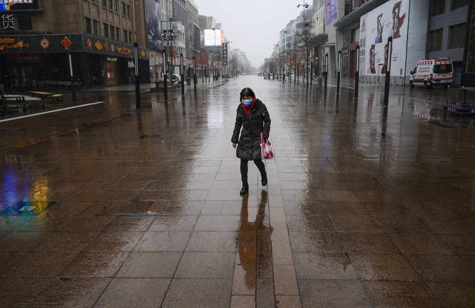  A Chinese woman walks through a nearly empty and shuttered commercial street following new lockdown measures