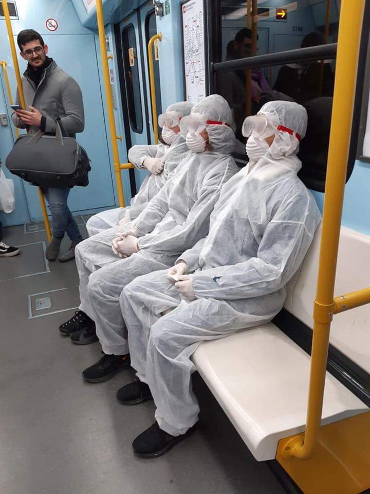  Three people wearing haz-mat style suits on the Milan metro